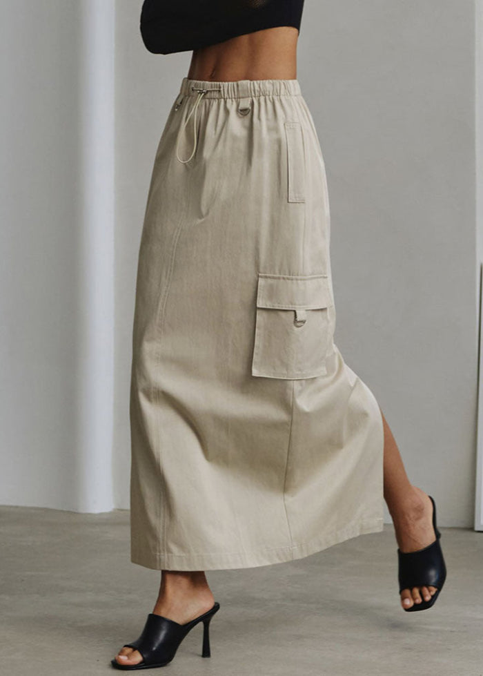 Beigefarbener Maxirock mit Seitentasche, kombiniert mit schwarzen High-Heels. Modetrend, Damenbekleidung, eleganter Look.