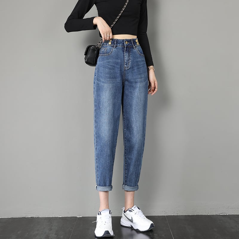 Frau in blauer Mom-Jeans, schwarzem Langarmshirt und weißen Sneakers vor grauer Wand. Modetrend, lässiger Stil, Damenmode, Streetwear.