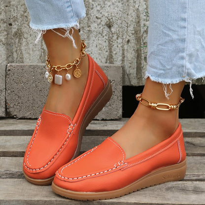 Orange Damen-Loafer aus Leder mit weißer Naht, kombiniert mit goldenen Fußkettchen und hellblauen Jeans. Modische Schuhe für den Sommer.
