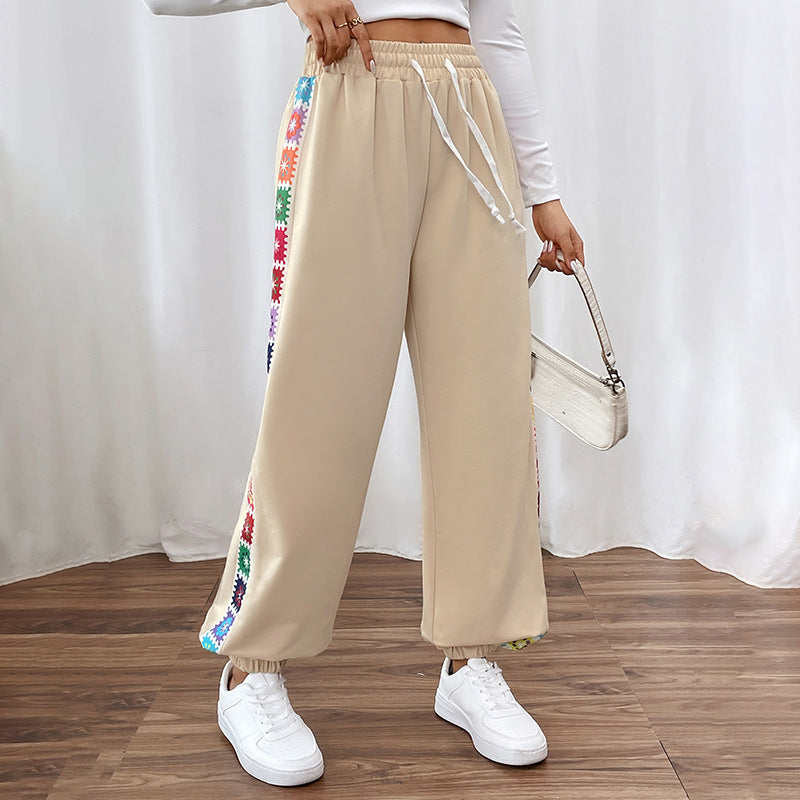 Damen Jogginghose beige mit bunten Streifen, kombiniert mit weißem Langarmshirt und Sneakers. Modetrend, Freizeitlook, bequeme Kleidung.