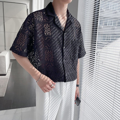 Mann in schwarzem, durchbrochenem Hemd und weißer Hose steht in modernem Raum. Stilvolle Herrenmode, Sommeroutfit, lässiger Look.