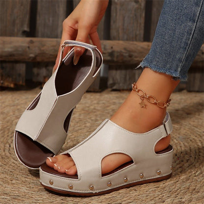 Beige Sandalen mit Keilabsatz und Nieten, getragen von einer Person mit Jeans und einem Stern-Armband. Modische Sommerschuhe für Damen.