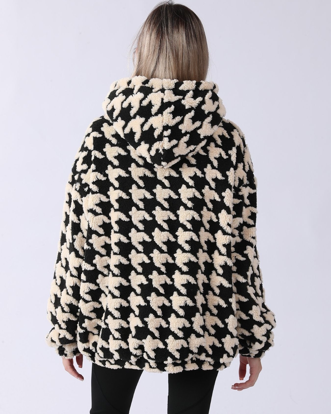 Frau in schwarz-weißem Hahnentritt-Mantel mit Kapuze, Rückansicht. Modetrend, Winterjacke, stilvolles Design, warme Oberbekleidung.