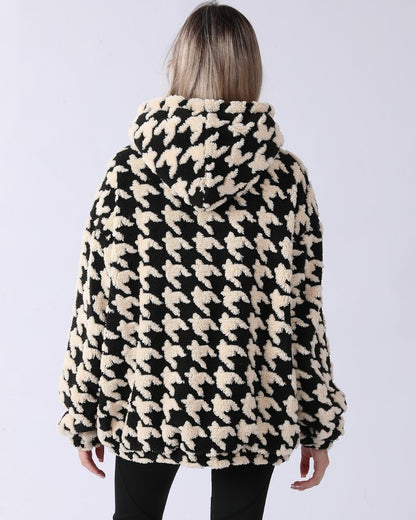 Frau in schwarz-weißem Hahnentritt-Mantel mit Kapuze, Rückansicht. Modetrend, Winterjacke, stilvolles Design, warme Oberbekleidung.