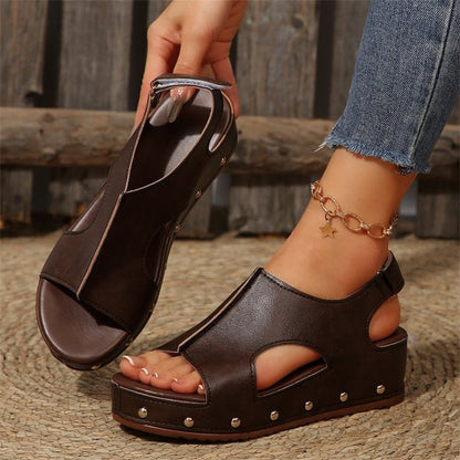 Braune Damen-Sandalen mit Keilabsatz und Nieten, getragen mit Jeans und einem goldenen Fußkettchen. Perfekt für Sommermode und Freizeitoutfits.