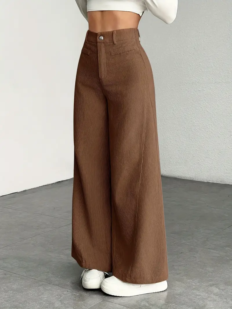 Braune Cordhose Damen, weites Bein, hohe Taille, kombiniert mit weißem Crop-Top und Sneakern, modischer Look, minimalistischer Hintergrund.