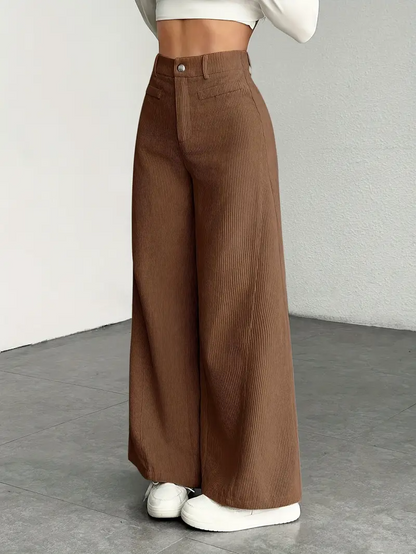 Braune Cordhose Damen, weites Bein, hohe Taille, kombiniert mit weißem Crop-Top und Sneakern, modischer Look, minimalistischer Hintergrund.