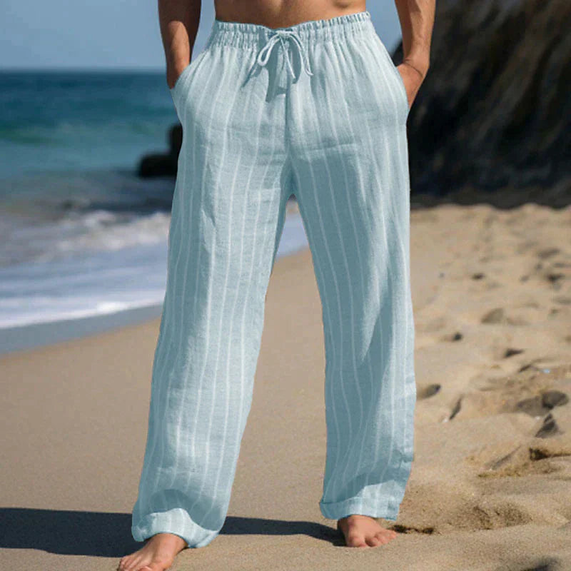 Person in hellblauer Leinenhose am Strand, entspannte Sommermode, lässige Strandkleidung, bequeme weite Hose, Urlaub am Meer.