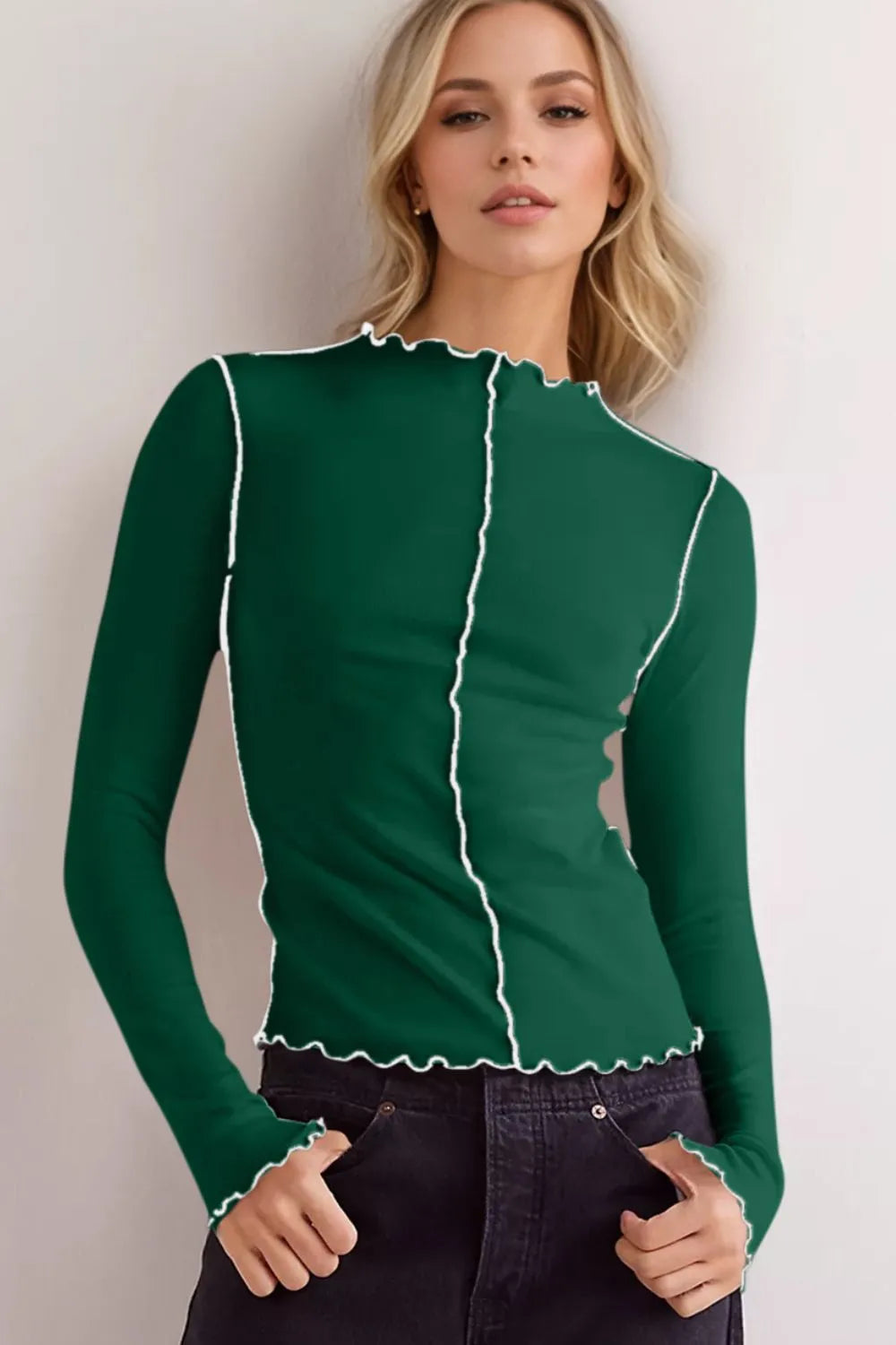 Frau in grünem Langarmshirt mit weißen Nähten, modisches Design, lässiger Look, blonde Haare, schwarze Hose, moderne Damenmode.