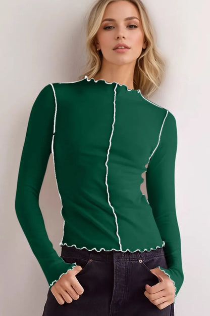 Frau in grünem Langarmshirt mit weißen Nähten, modisches Design, lässiger Look, blonde Haare, schwarze Hose, moderne Damenmode.