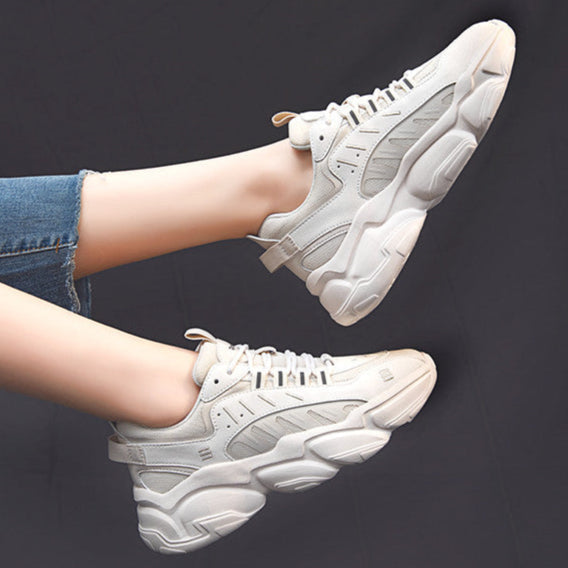 Weiße Chunky Sneaker an Füßen, die in blauen Jeans stecken, vor schwarzem Hintergrund. Modische, bequeme Turnschuhe für Damen.