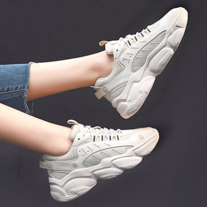 Weiße Chunky Sneaker an Füßen, die in blauen Jeans stecken, vor schwarzem Hintergrund. Modische, bequeme Turnschuhe für Damen.