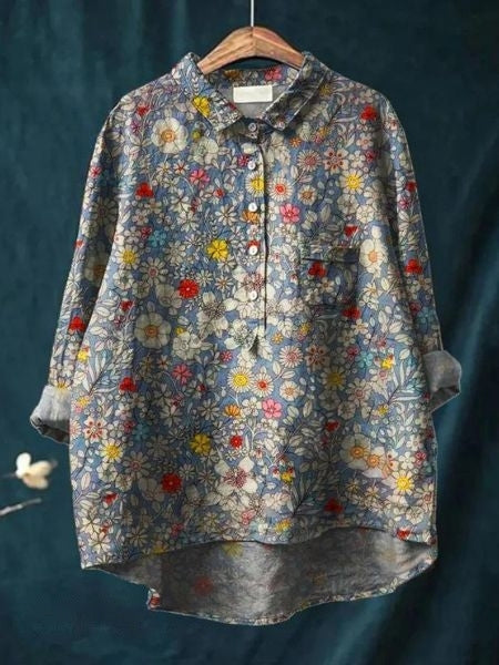 Bluse mit Blumenmuster, langärmlig, aus Baumwolle, auf einem Kleiderbügel vor dunkelblauem Hintergrund. Vintage-Stil, modisch, Damenbekleidung.