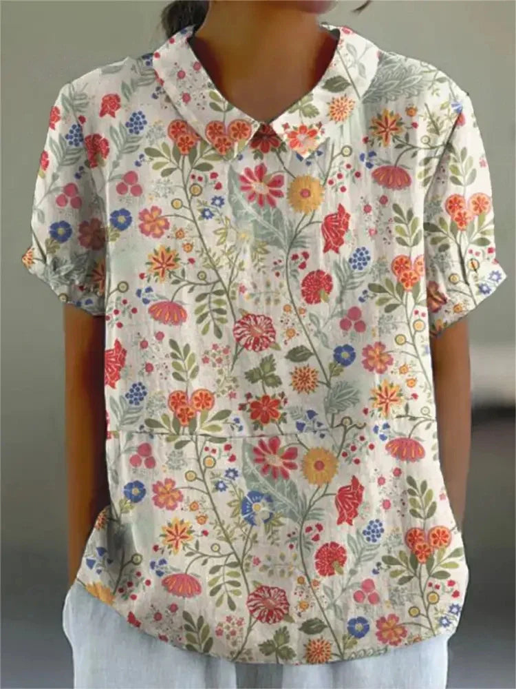 Frau trägt kurzärmlige Bluse mit buntem Blumenmuster, Kragen und Knopfleiste. Modische Damenbekleidung, florales Design, Sommerlook.