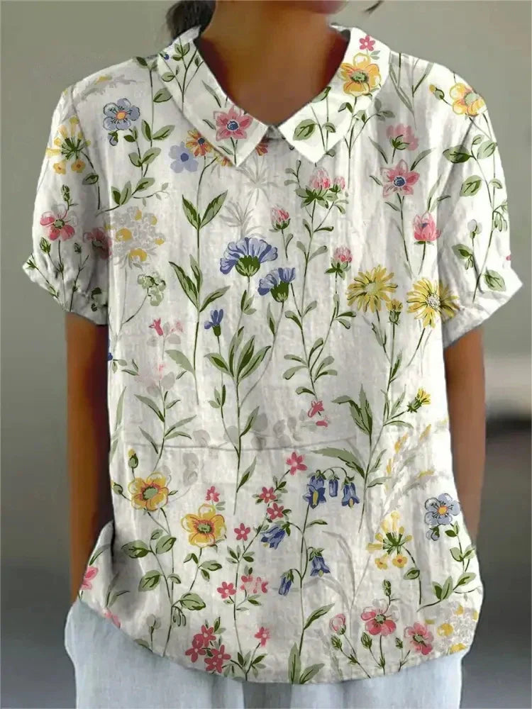 Damenbluse mit Blumenmuster, kurzärmelig, weißer Hintergrund, bunte Blumen, lässiger Stil, modische Sommerbekleidung, florales Design.