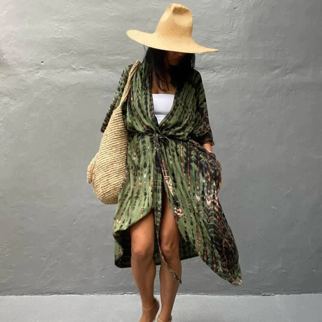 Frau in grünem Kaftan mit Strohhut und Strohtasche vor grauer Wand. Sommermode, Boho-Stil, lässiger Look.