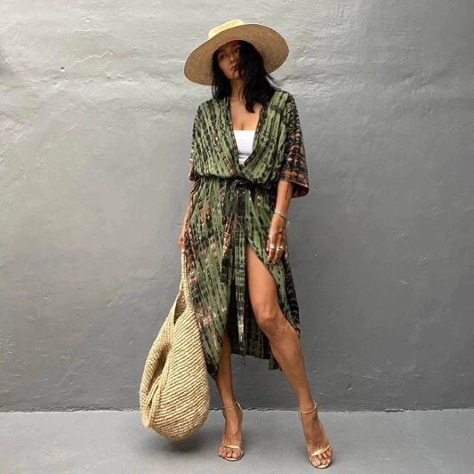 Frau in grünem Kimono-Kleid mit Strohhut und Sandalen, hält eine große Strohtasche. Sommermode, Boho-Stil, lässiger Look.