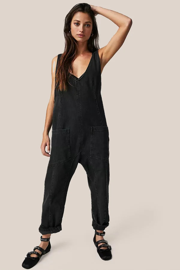Frau in schwarzem Denim-Jumpsuit mit V-Ausschnitt und Taschen, lässiger Look, modische Damenbekleidung, trendiger Einteiler, schwarze Schuhe.