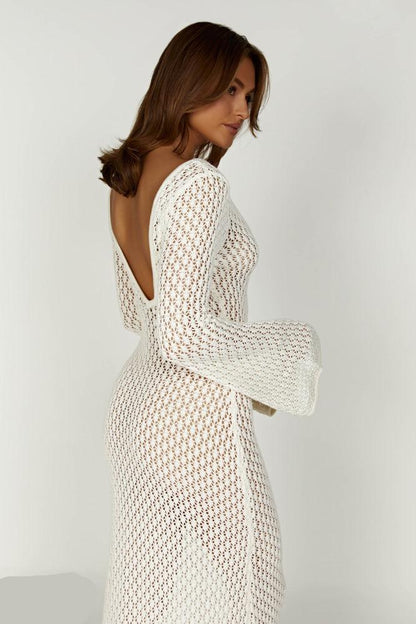 Frau in weißem, gehäkeltem Kleid mit tiefem Rückenausschnitt, seitlich fotografiert. Elegante Mode, Sommerkleid, Damenbekleidung.