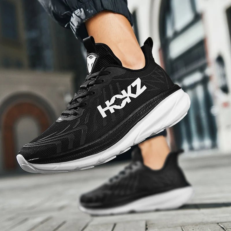 Schwarzer Sportschuh mit weißer Sohle und HOKZ-Logo, getragen von einer Person auf städtischem Hintergrund. Ideal für Laufen und Fitness.