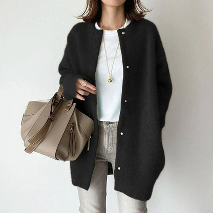 Frau in schwarzem Cardigan, weißem T-Shirt und grauer Hose, hält beige Handtasche. Modischer Herbst-Look, lässig und elegant.