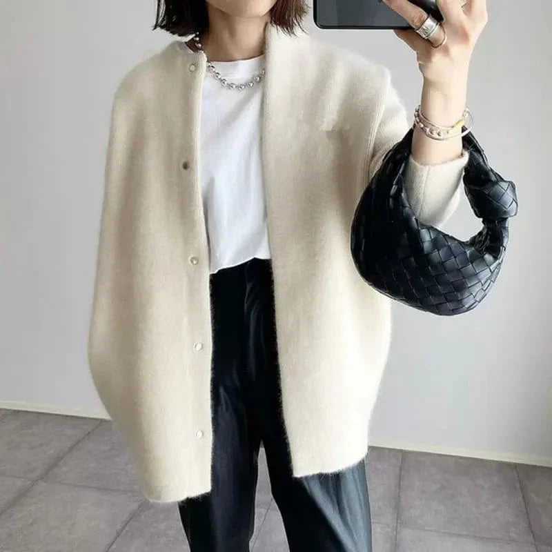 Dame in weißem Cardigan und schwarzer Hose, hält schwarze geflochtene Handtasche. Modetrend, eleganter Look, minimalistisch, Streetstyle.