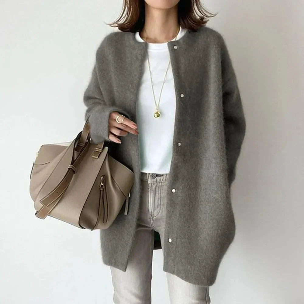 Frau in grauem Strickmantel, weißem T-Shirt und Jeans, hält beige Handtasche. Modetrend, Herbstmode, lässiger Stil.