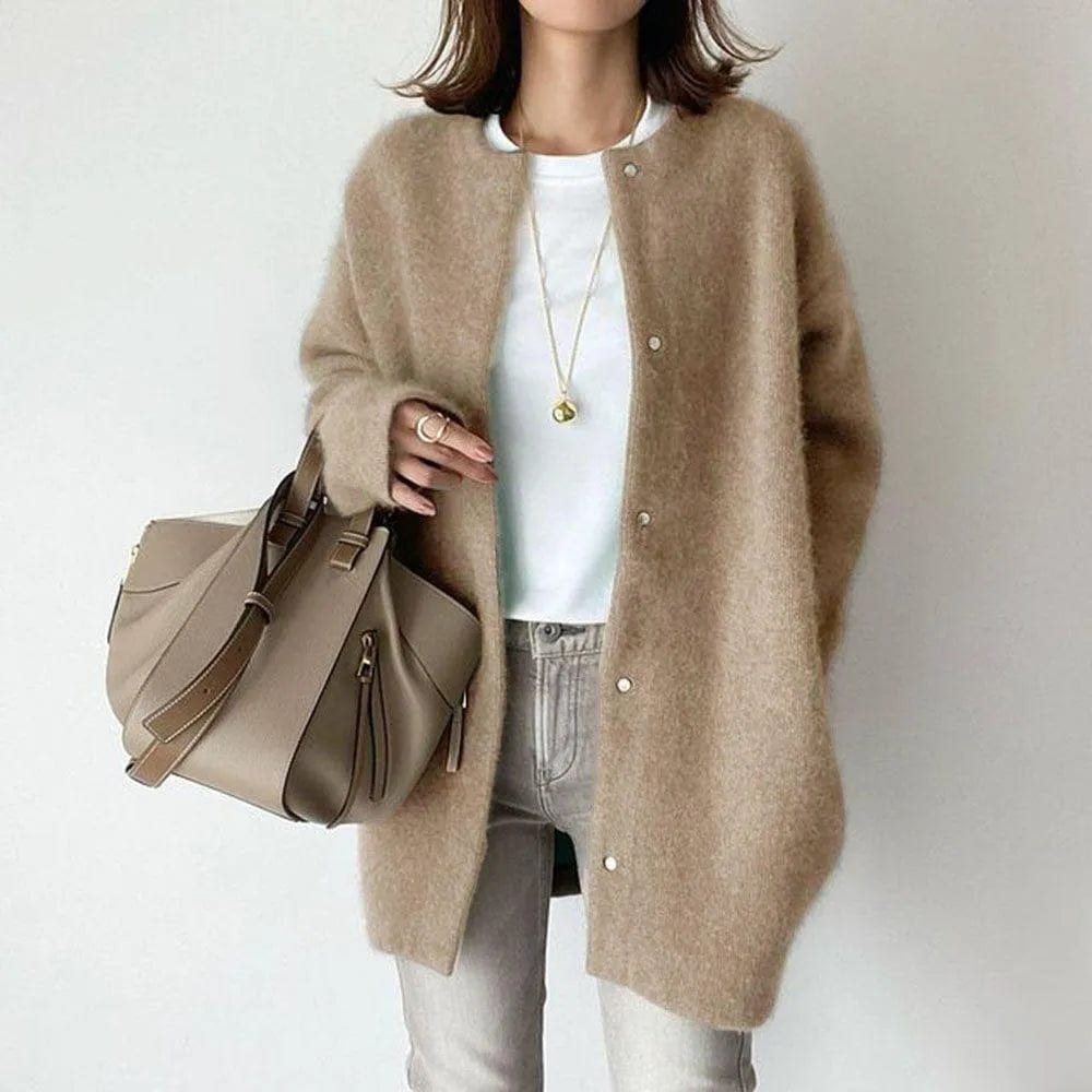 Frau in beigem Strickmantel, weißem T-Shirt und Jeans, hält eine beige Handtasche. Modetrend, Herbstmode, Damenbekleidung, lässiger Stil.