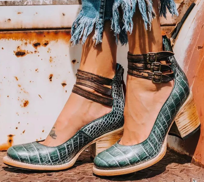 Grüne Krokodilleder-Absatzschuhe mit doppelten Riemen, getragen von einer Person in zerrissenen Jeans. Modische Damenschuhe, Vintage-Stil.