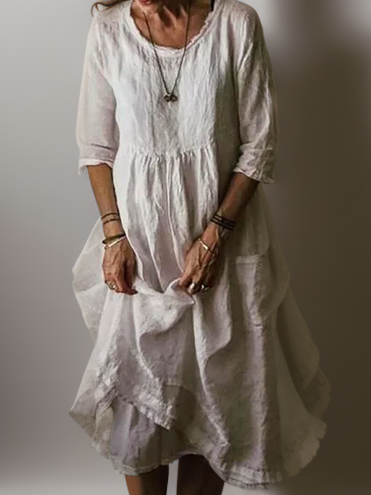 Frau in weißem Leinenkleid, knielang, mit Dreiviertelärmeln. Sommermode, lässiger Boho-Stil, ideal für warme Tage. Elegantes, luftiges Design.