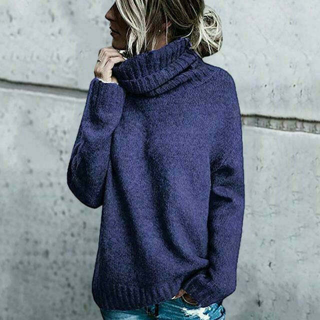 Frau in blauem Rollkragenpullover vor grauer Wand, lässiger Winterlook, modischer Strickpullover, gemütliche Damenmode, Herbst-Winter-Outfit.