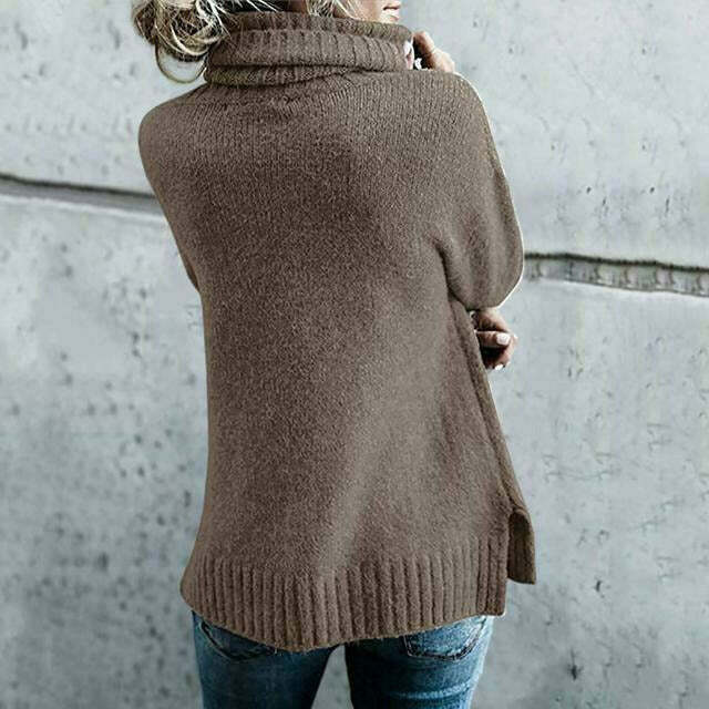 Frau in braunem Rollkragenpullover und blauer Jeans vor grauer Wand. Modetrend, Herbstmode, Strickpullover, lässiger Stil.
