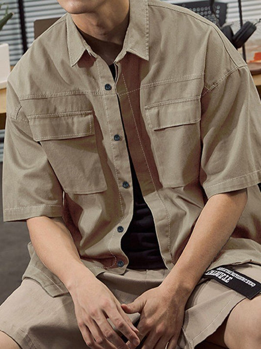 Mann in beigem Kurzarmhemd und Shorts sitzt, modernes Freizeitoutfit, Sommermode, lässiger Stil, Herrenbekleidung, urbaner Look.