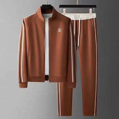 Brauner Trainingsanzug mit weißen Streifen, bestehend aus Jacke und Hose, auf grauem Hintergrund. Sportbekleidung, Freizeitmode, Herrenanzug.
