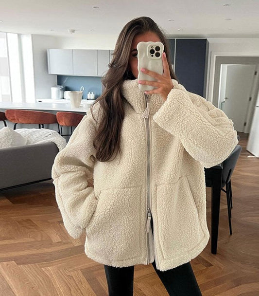 Frau in weißer Teddyjacke macht Selfie in modernem Wohnzimmer. Wintermode, gemütliche Kleidung, Innenraum, Smartphone, modischer Look.