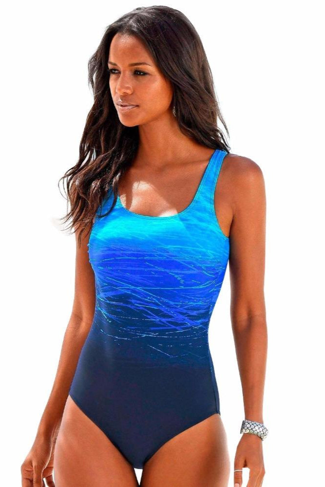 Frau in blauem Badeanzug mit Wasserwellenmuster, stehend vor weißem Hintergrund. Sommermode, Strandbekleidung, Damenbadeanzug.