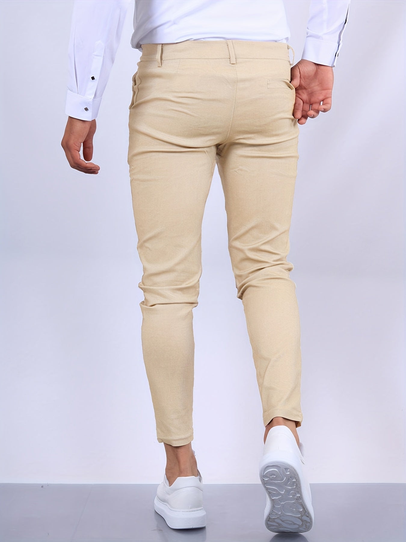 Mann in beiger Chinohose und weißem Hemd, von hinten fotografiert, geht auf grauem Boden. Elegante Herrenmode, Freizeitlook, stilvolle Kleidung.