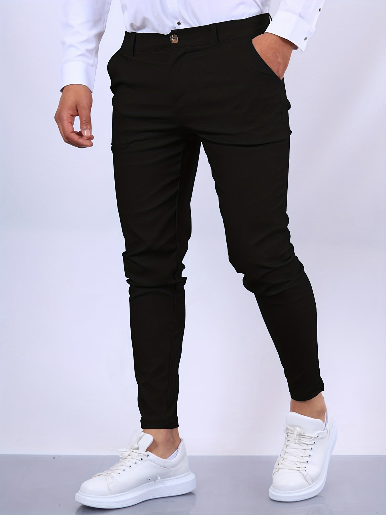 Mann in schwarzer Chinohose und weißen Sneakers, modisch gekleidet, vor neutralem Hintergrund. Elegante Herrenmode, Freizeitlook.