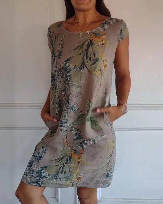 Frau trägt ein knielanges, florales Sommerkleid mit Taschen. Das Kleid hat ein botanisches Muster in Grün- und Brauntönen.