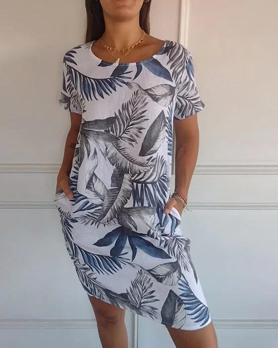 Frau trägt ein sommerliches Kleid mit blau-weißem tropischem Blattmuster, kurze Ärmel, knielang, lässiger Stil, ideal für warme Tage.