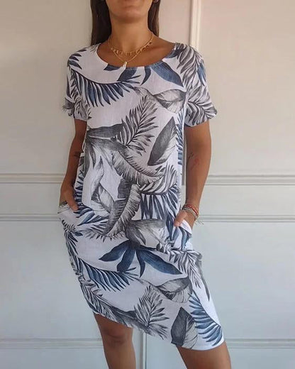 Frau trägt ein sommerliches Kleid mit blau-weißem tropischem Blattmuster, kurze Ärmel, knielang, lässiger Stil, ideal für warme Tage.