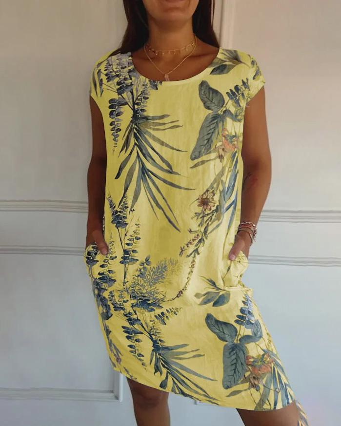 Frau trägt gelbes Sommerkleid mit tropischem Blumenmuster, kurze Ärmel, Taschen, lässiger Stil. Perfekt für Strandmode und Sommeroutfits.