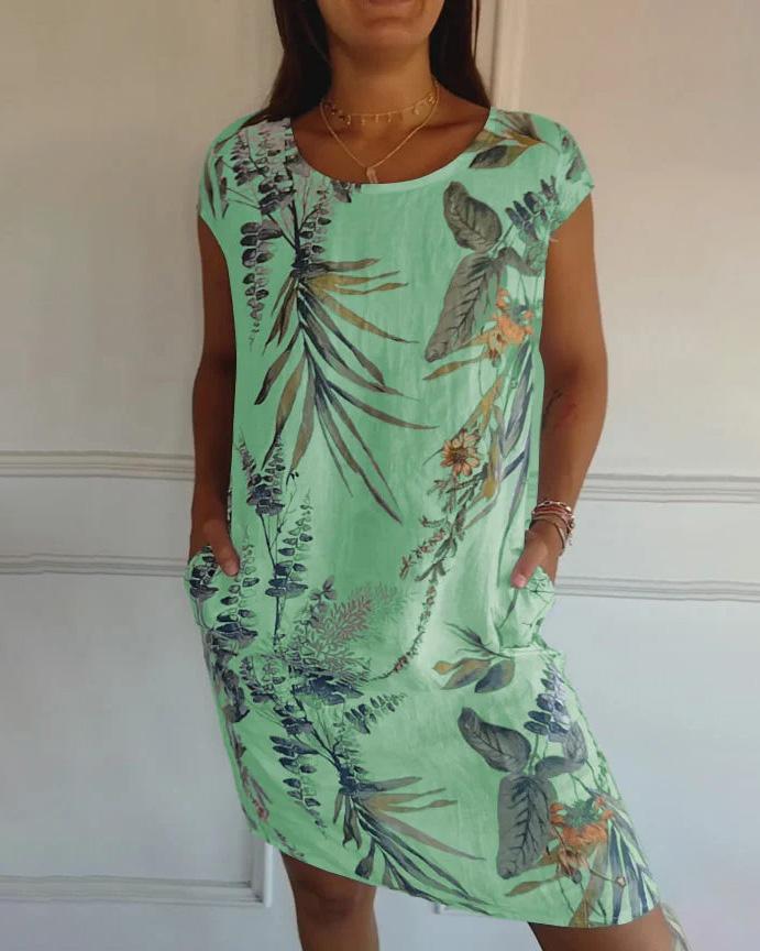 Frau trägt mintgrünes Sommerkleid mit tropischem Blumenmuster, kurzen Ärmeln und Taschen. Perfekt für Strandmode und Freizeitkleidung.