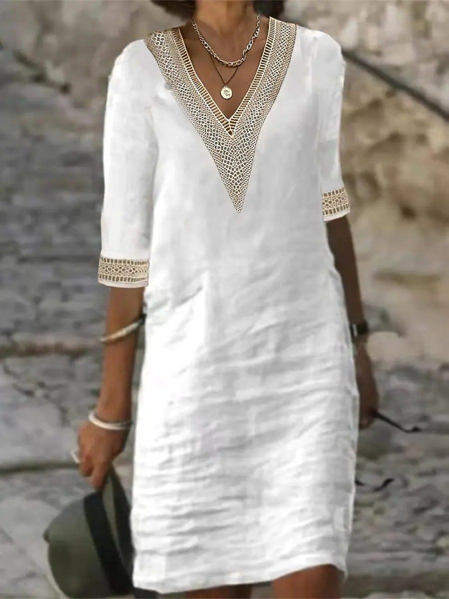Frau in weißem Leinenkleid mit V-Ausschnitt und Spitzenbesatz, gehend auf Kopfsteinpflaster. Sommermode, elegantes Design, Freizeitkleidung.