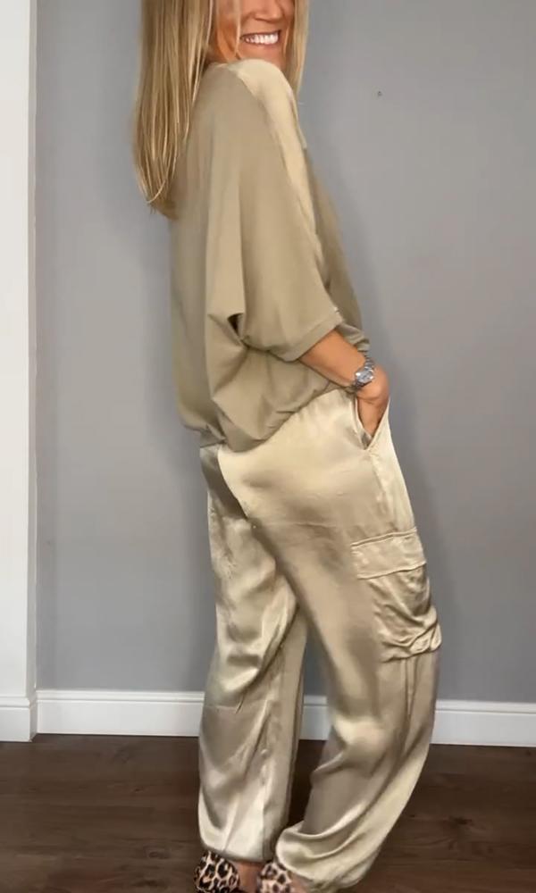 Frau in beiger Satinbluse und -hose, lächelnd, seitlich stehend, mit Leopardenmuster-Schuhen. Elegante Mode, lässiger Stil, Innenaufnahme.