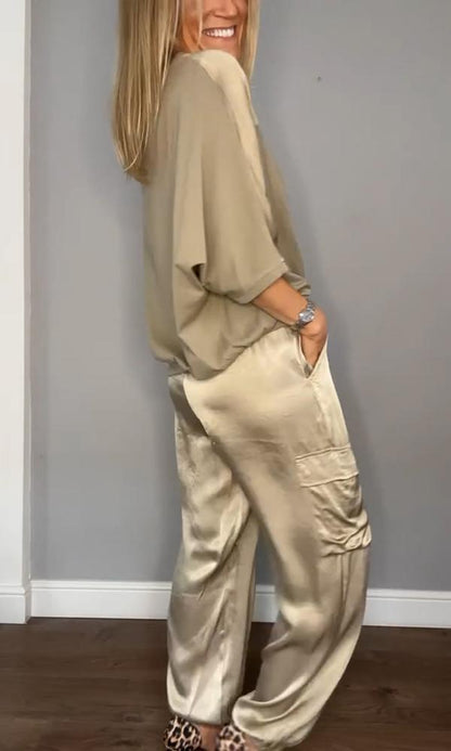 Frau in beiger Satinbluse und -hose, lächelnd, seitlich stehend, mit Leopardenmuster-Schuhen. Elegante Mode, lässiger Stil, Innenaufnahme.