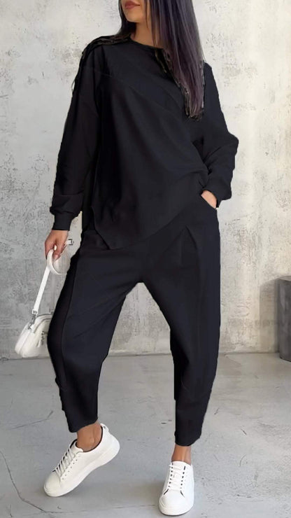 Frau in schwarzem Oversize-Sweatshirt und Jogginghose, weiße Sneakers, weiße Handtasche, grauer Betonhintergrund. Modetrend, lässiger Stil.