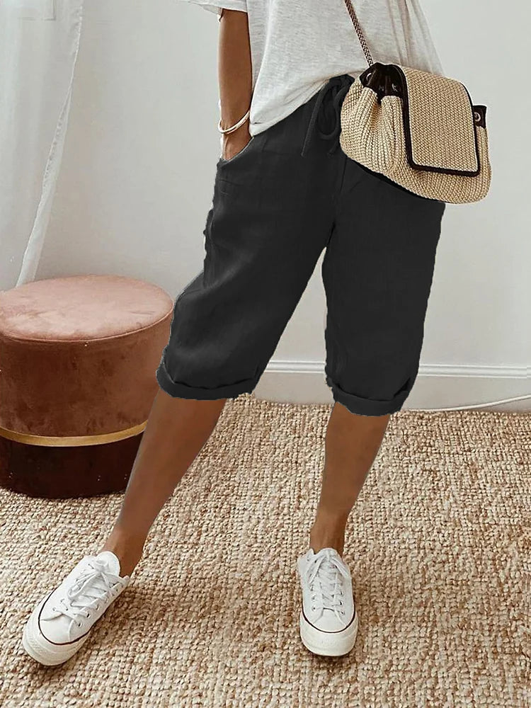 Frau in lässiger Sommermode mit weißem T-Shirt, schwarzen Bermuda-Shorts und weißen Sneakers. Strohtasche als Accessoire. Perfekt für Freizeit und Alltag.