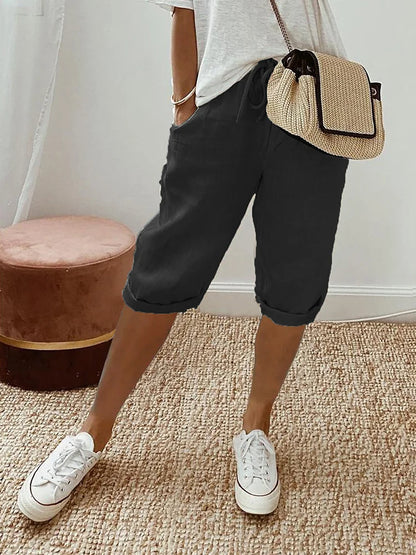 Frau in lässiger Sommermode mit weißem T-Shirt, schwarzen Bermuda-Shorts und weißen Sneakers. Strohtasche als Accessoire. Perfekt für Freizeit und Alltag.