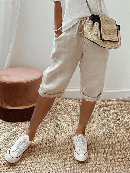 Frau in beiger Leinenhose und weißen Sneakers, trägt eine beige Umhängetasche. Modetrend, Sommeroutfit, lässiger Stil.